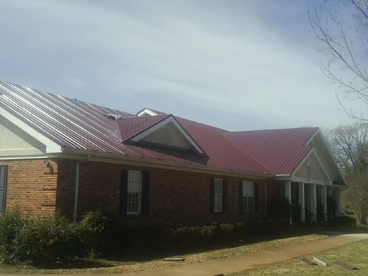 Red metal roof with gabled entries on a long brick building, from a Hail Damage Roof Repair job in Cook