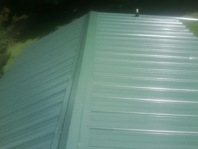 New green metal panels meeting at the ridge of a roof — Flat Roof Repair work by our crew in Cook