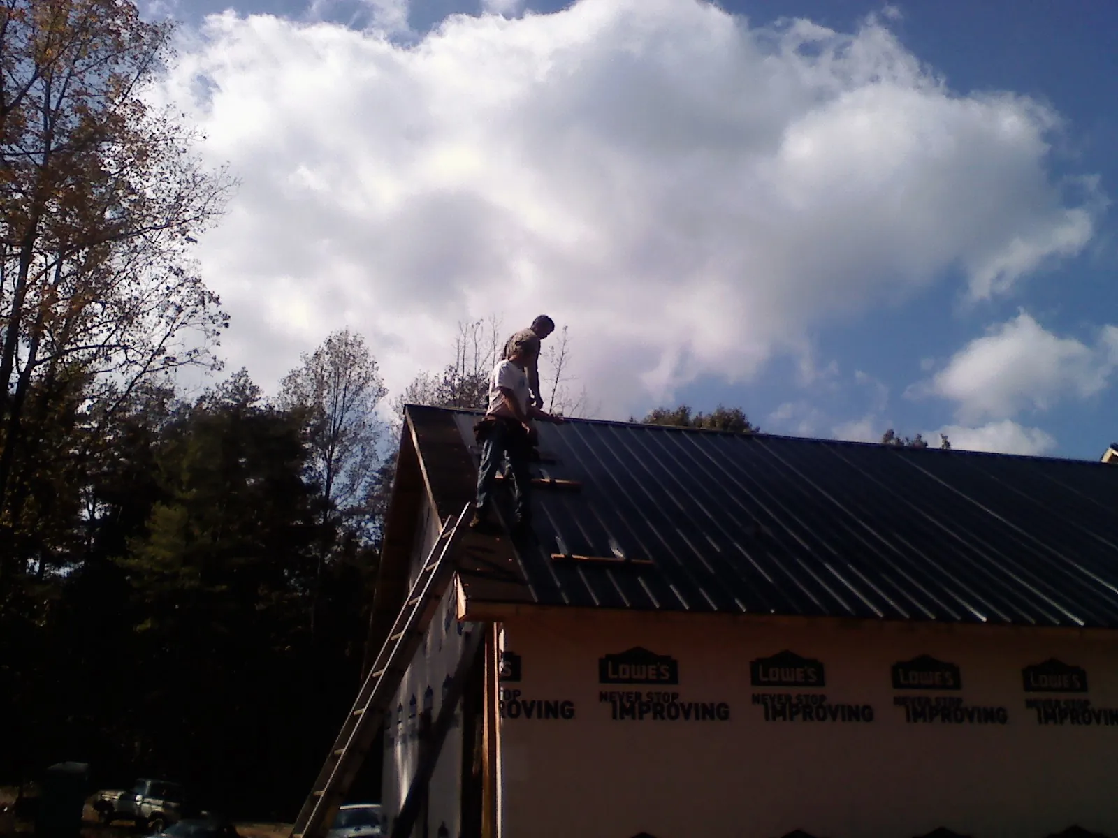 Roofer fastening dark metal panels high against a cloudy sky, from a Roof Inspection job in Cook